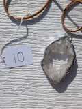 Front of Open Sky geode necklace No. 010, showing its natural crystal and stone pattern, handmade silver-tone edge, and tan cord.