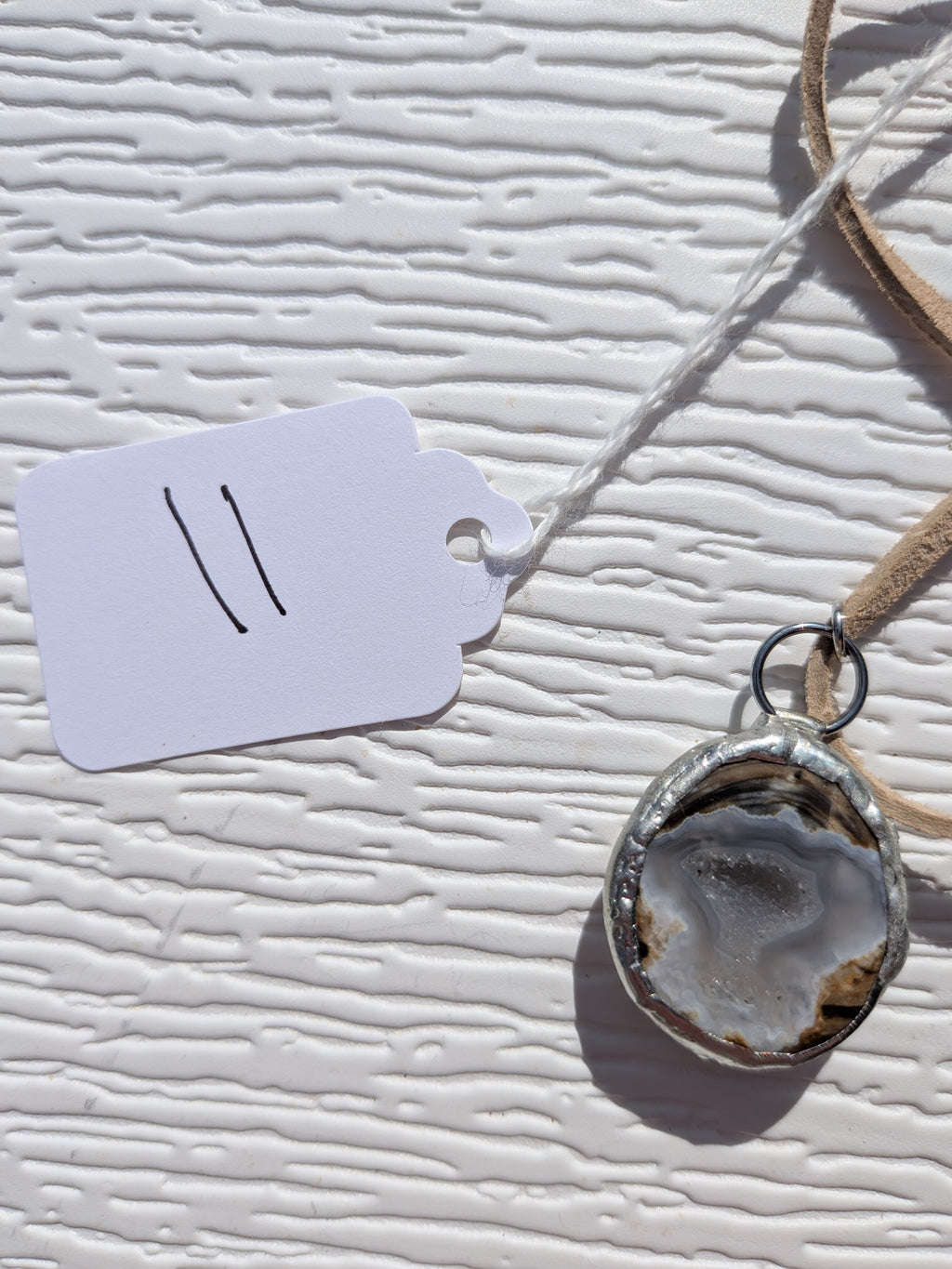 Front of Silver Mist Banded necklace No. 011, showing its natural stone pattern, handmade silver-tone edge, and tan cord.