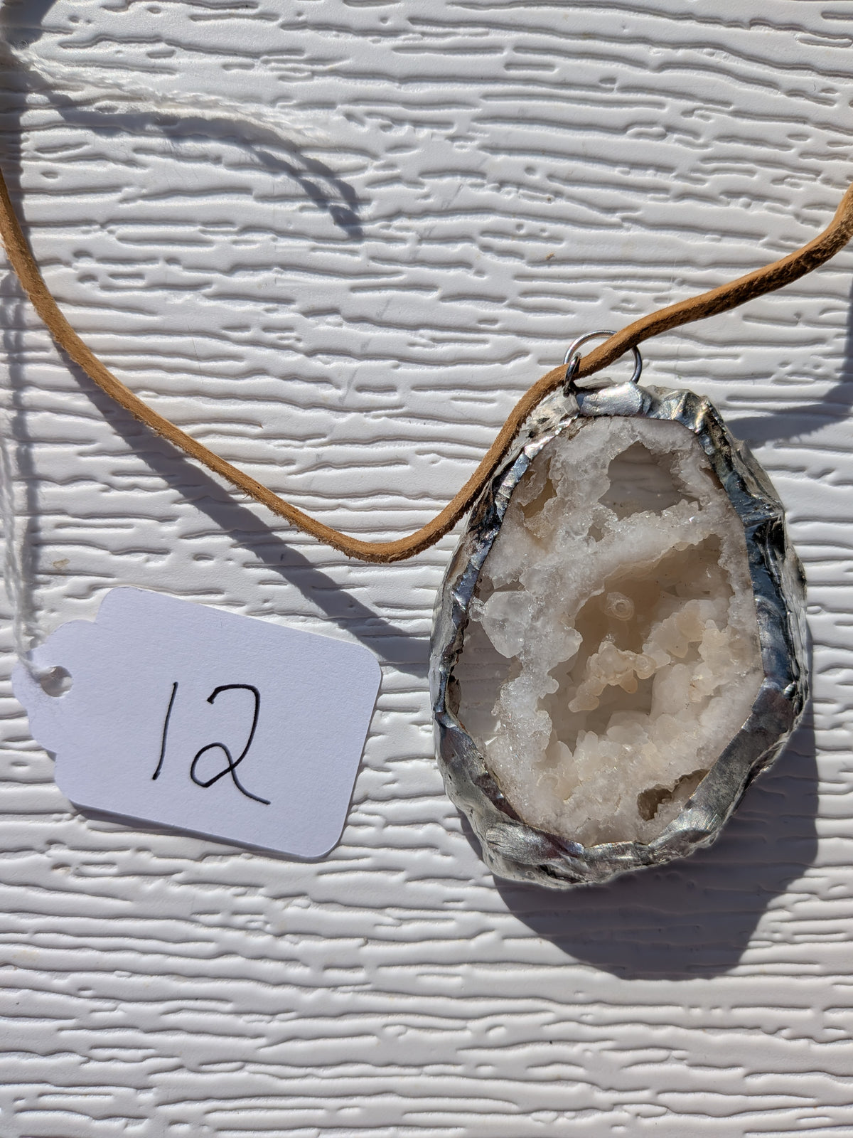 Front of Honey Crystal Cavern geode necklace No. 012, showing its natural crystal and stone pattern, handmade silver-tone edge, and tan cord.
