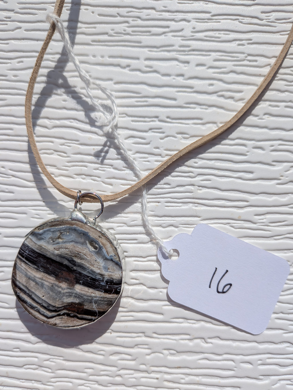 Front of River Strata necklace No. 016, showing its natural stone pattern, handmade silver-tone edge, and tan cord.