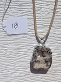 Front of Crystal Grotto necklace No. 018, showing its natural stone pattern, handmade silver-tone edge, and tan cord.