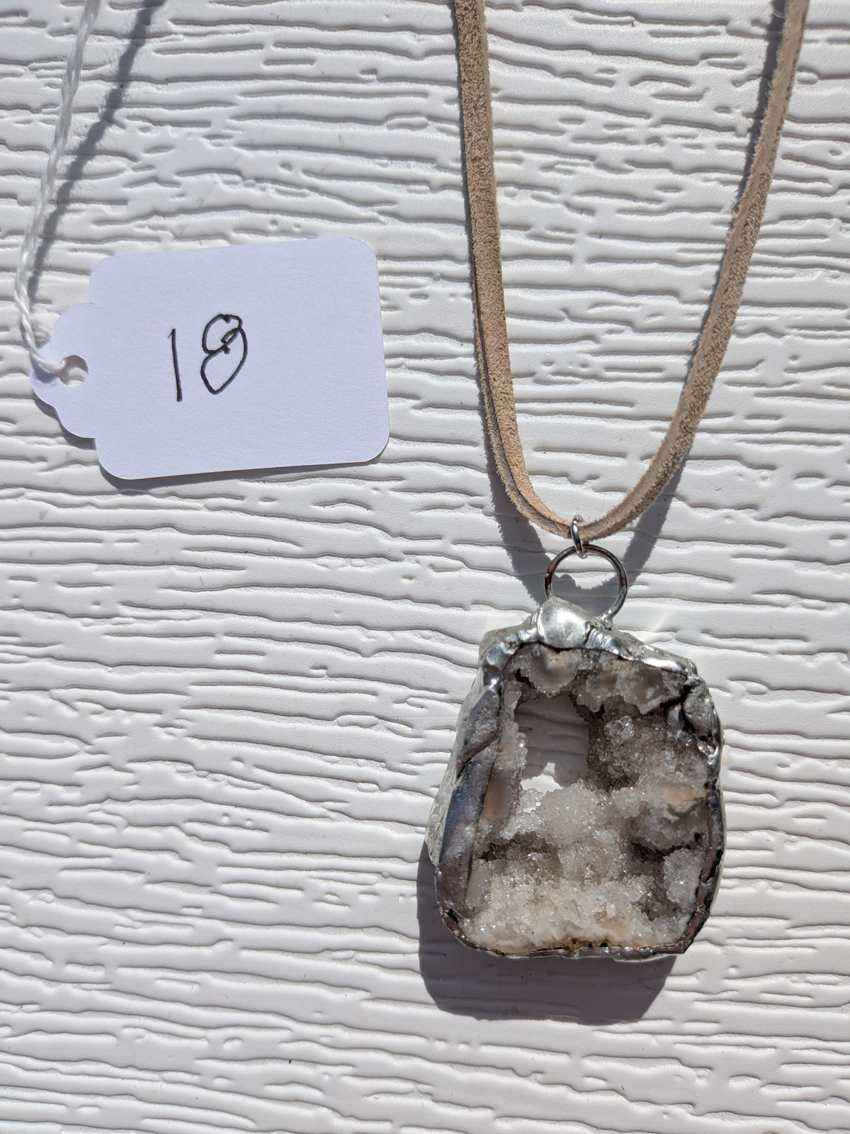 Front of Crystal Grotto necklace No. 018, showing its natural stone pattern, handmade silver-tone edge, and tan cord.
