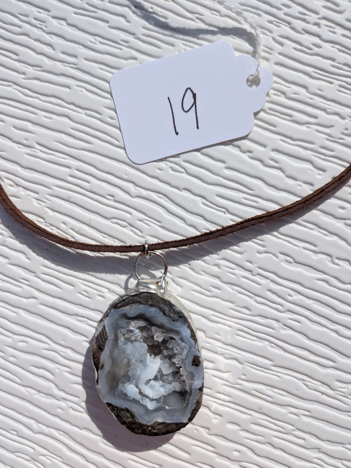 Front of Storm Crystal Cavern necklace No. 019, showing its natural stone pattern, handmade silver-tone edge, and dark brown cord.