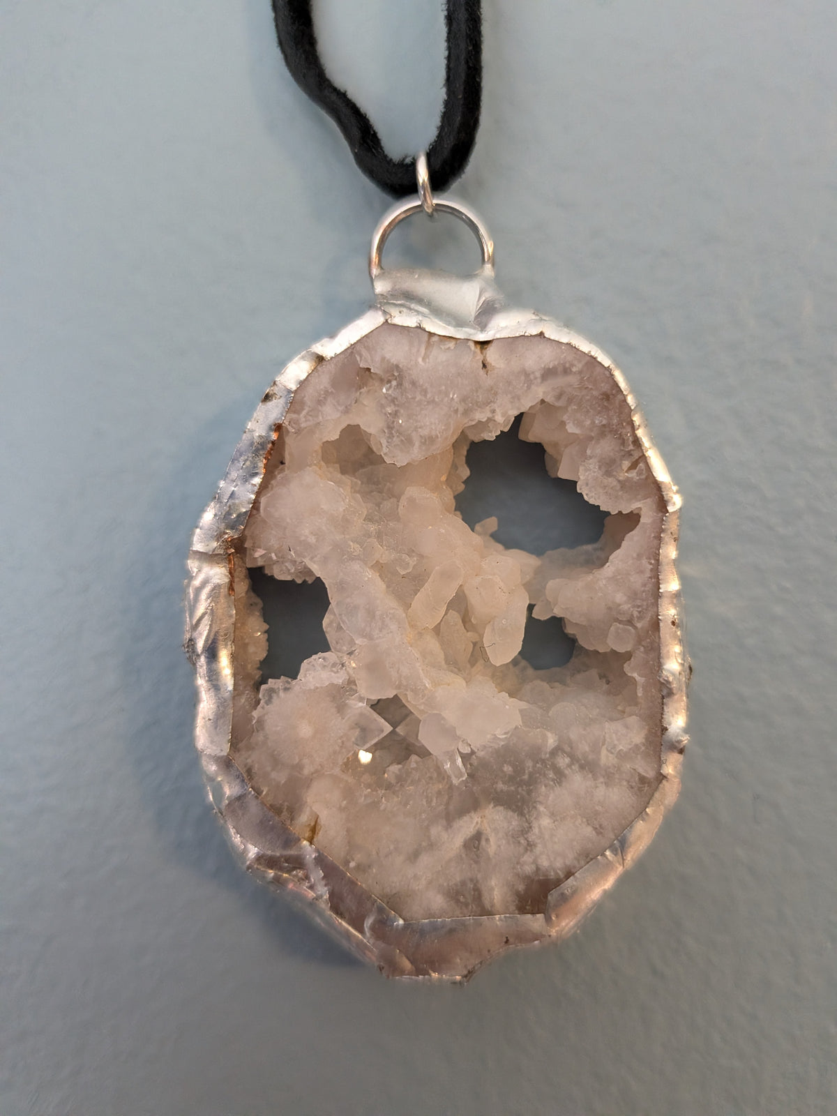 Necklace No. 001: front close-up of the cream geode, crystal openings, silver-tone edging and black cord.