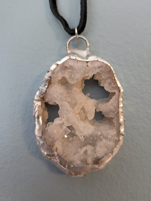 Necklace No. 001: front close-up of the cream geode, crystal openings, silver-tone edging and black cord.