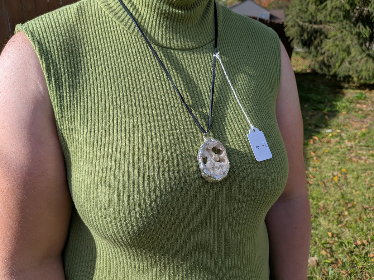 Crystal Cavern geode necklace No. 001 worn over a green top, showing the pendant’s proportions and black cord.