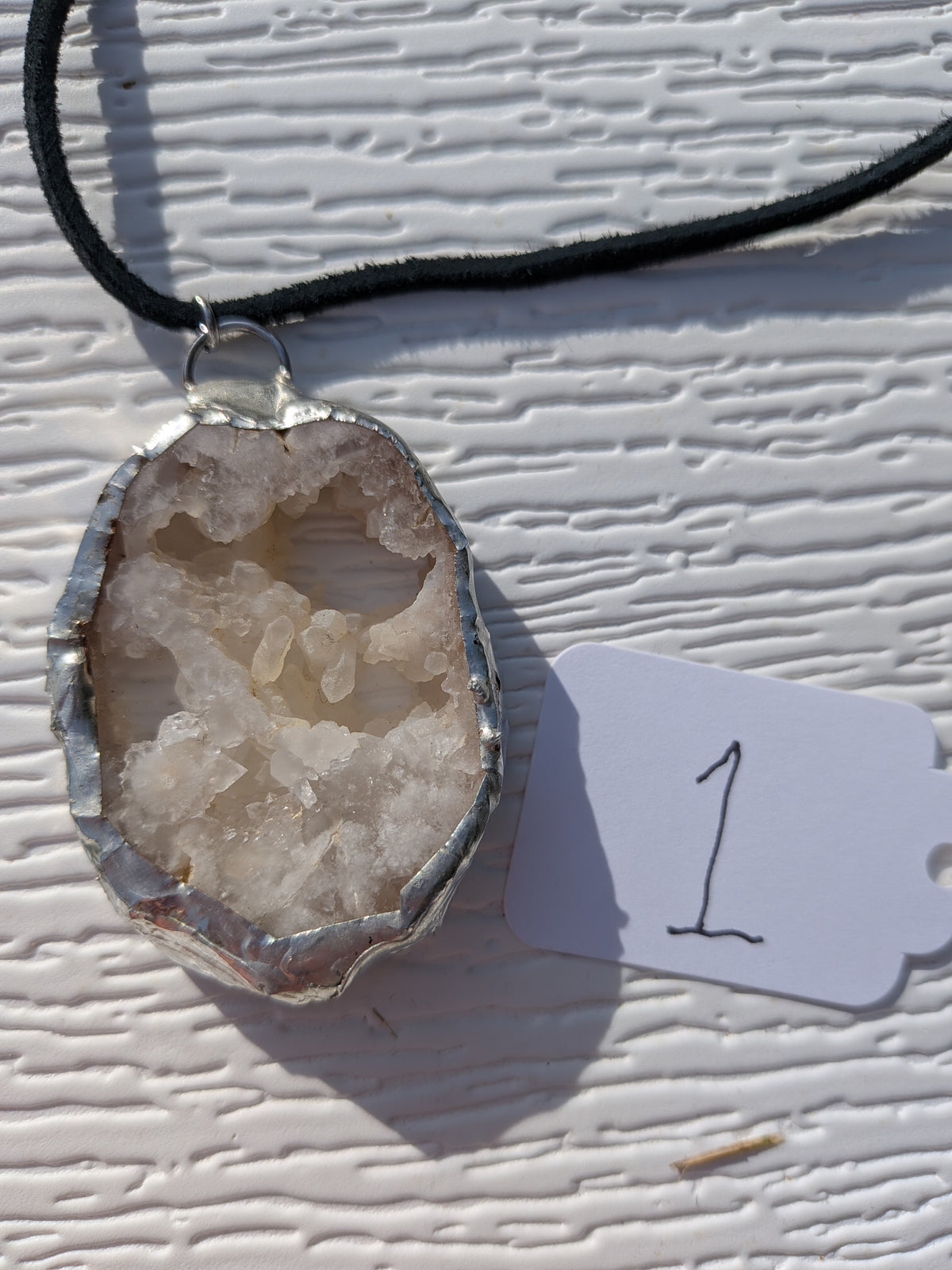 Front of Crystal Cavern geode necklace No. 001, with creamy white crystals, natural openings, silver-tone edging, and a black cord.