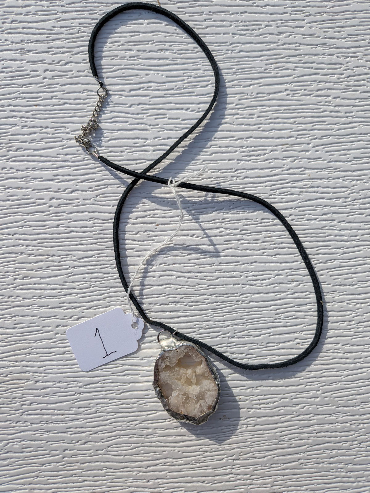 Full Crystal Cavern geode necklace No. 001, showing the white crystal pendant, black cord, clasp, and extension chain.
