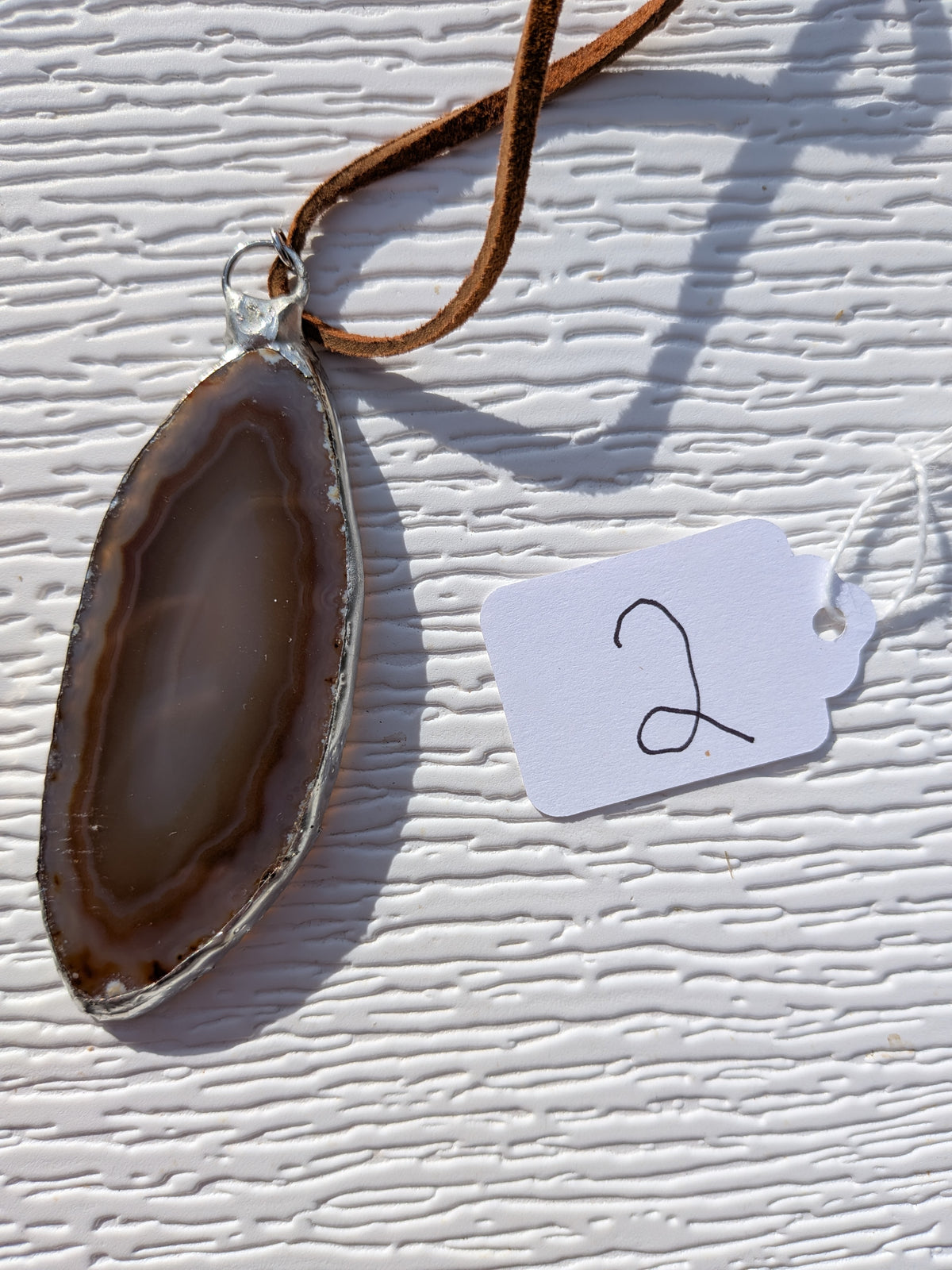 Back of Earthline Banded geode necklace No. 002, showing its smooth banded stone face and handmade silver-tone edge.