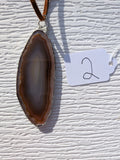 Front of Earthline Banded geode necklace No. 002, with brown concentric bands, a smoky-gray center, handmade silver-tone edging, and brown cord.