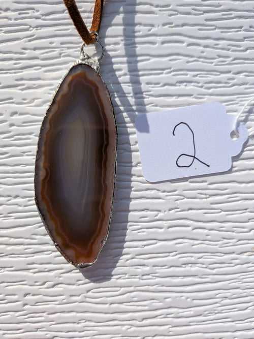 Front of Earthline Banded geode necklace No. 002, with brown concentric bands, a smoky-gray center, handmade silver-tone edging, and brown cord.