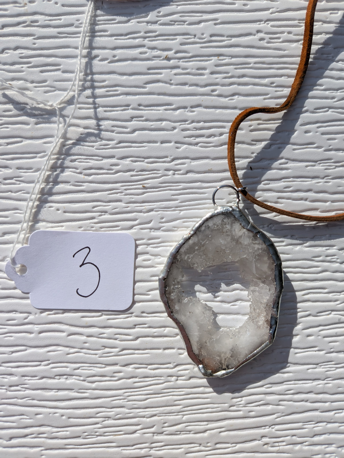 Front of Crystal Window geode necklace No. 003, with a pale crystal-lined opening, gray stone, handmade silver-tone edge, and tan cord.