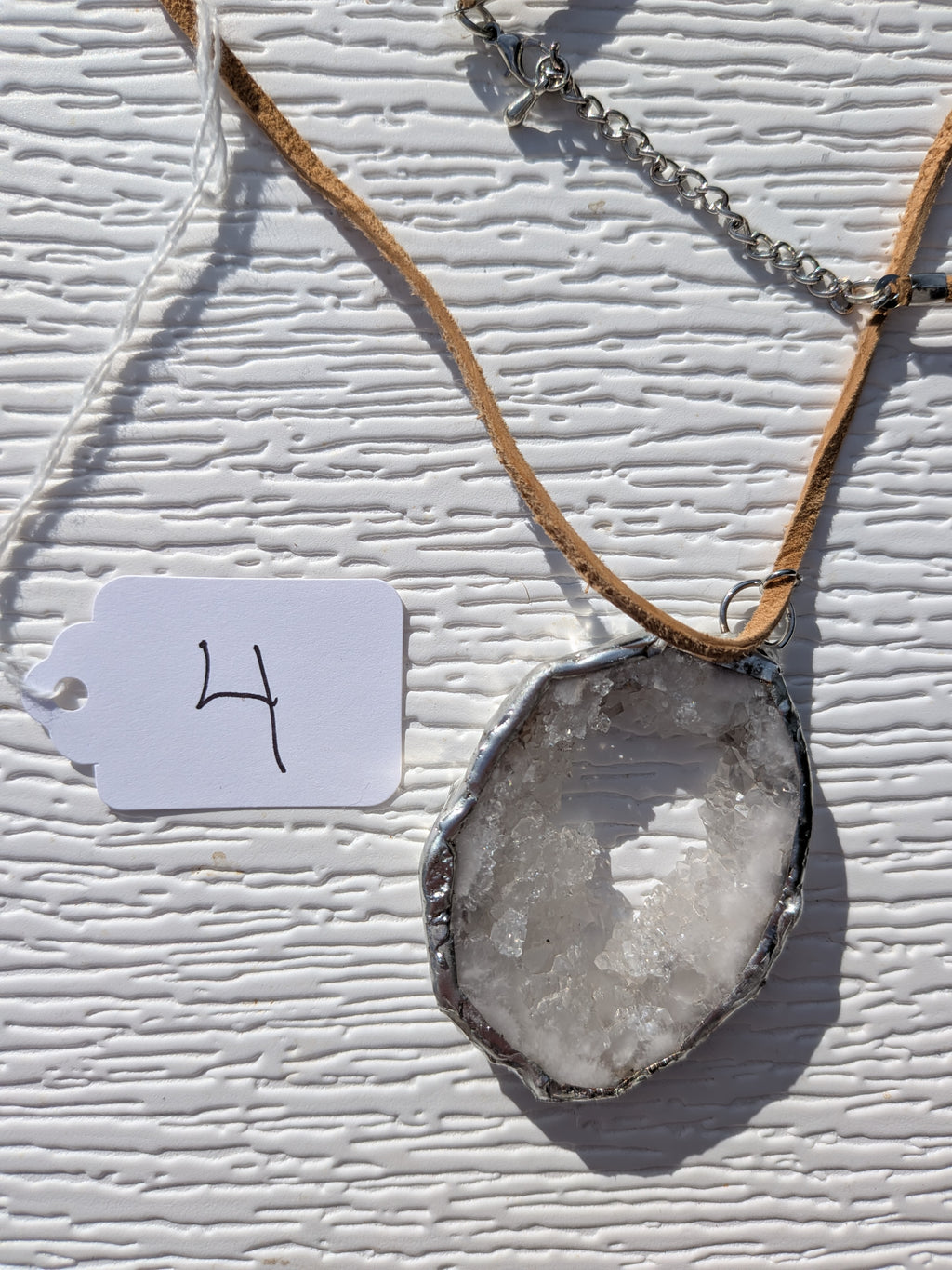 Front of Frosted Halo geode necklace No. 004, showing its natural crystal and stone pattern, handmade silver-tone edge, and tan cord.