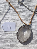Front of Frosted Halo geode necklace No. 004, showing its natural crystal and stone pattern, handmade silver-tone edge, and tan cord.