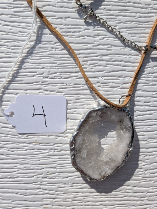 Front of Frosted Halo geode necklace No. 004, showing its natural crystal and stone pattern, handmade silver-tone edge, and tan cord.