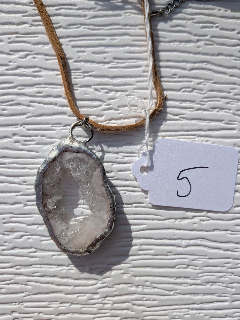Front of Dewdrop Window geode necklace No. 005, showing its natural crystal and stone pattern, handmade silver-tone edge, and tan cord.