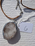 Front of Frosted Crystal geode necklace No. 006, showing its natural crystal and stone pattern, handmade silver-tone edge, and brown cord.