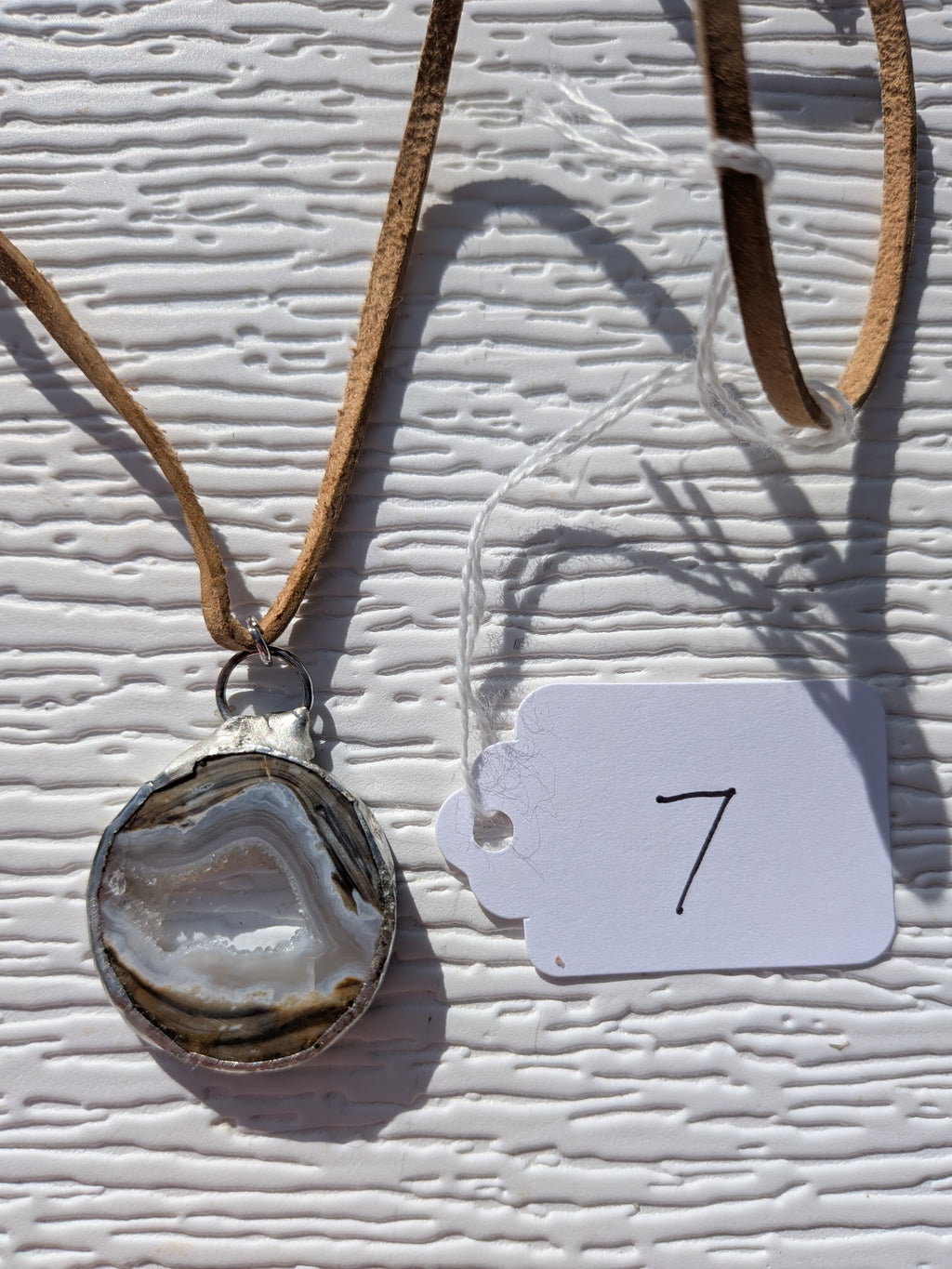 Front of Earth Rings geode necklace No. 007, showing its natural crystal and stone pattern, handmade silver-tone edge, and tan cord.