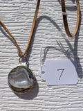 Front of Earth Rings geode necklace No. 007, showing its natural crystal and stone pattern, handmade silver-tone edge, and tan cord.