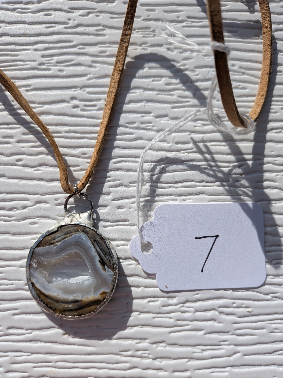 Front of Earth Rings geode necklace No. 007, showing its natural crystal and stone pattern, handmade silver-tone edge, and tan cord.