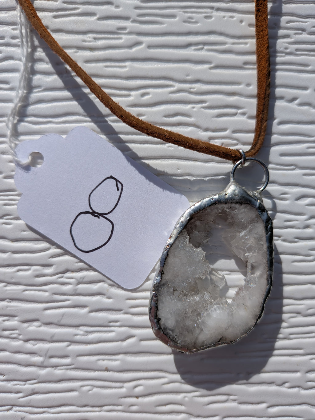 Front of Little Crystal Window geode necklace No. 008, showing its natural crystal and stone pattern, handmade silver-tone edge, and brown cord.