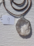 Front of Crystal Bridge geode necklace No. 009, showing its natural crystal and stone pattern, handmade silver-tone edge, and dark brown cord.