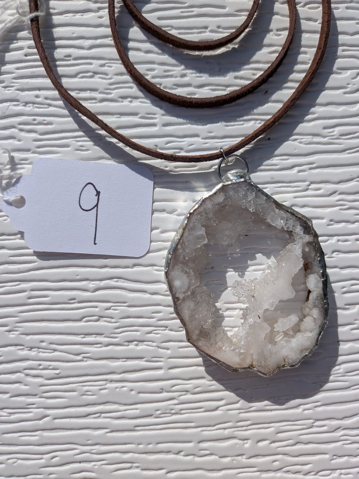 Front of Crystal Bridge geode necklace No. 009, showing its natural crystal and stone pattern, handmade silver-tone edge, and dark brown cord.
